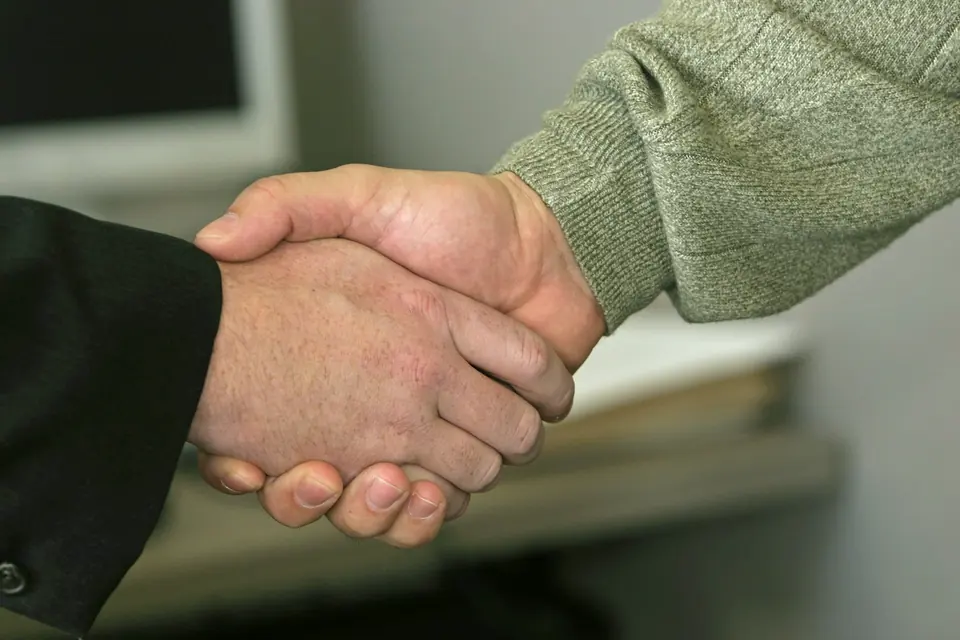 Håndtrykk mellom en person i dressjakke og en i grønn strikkegenser